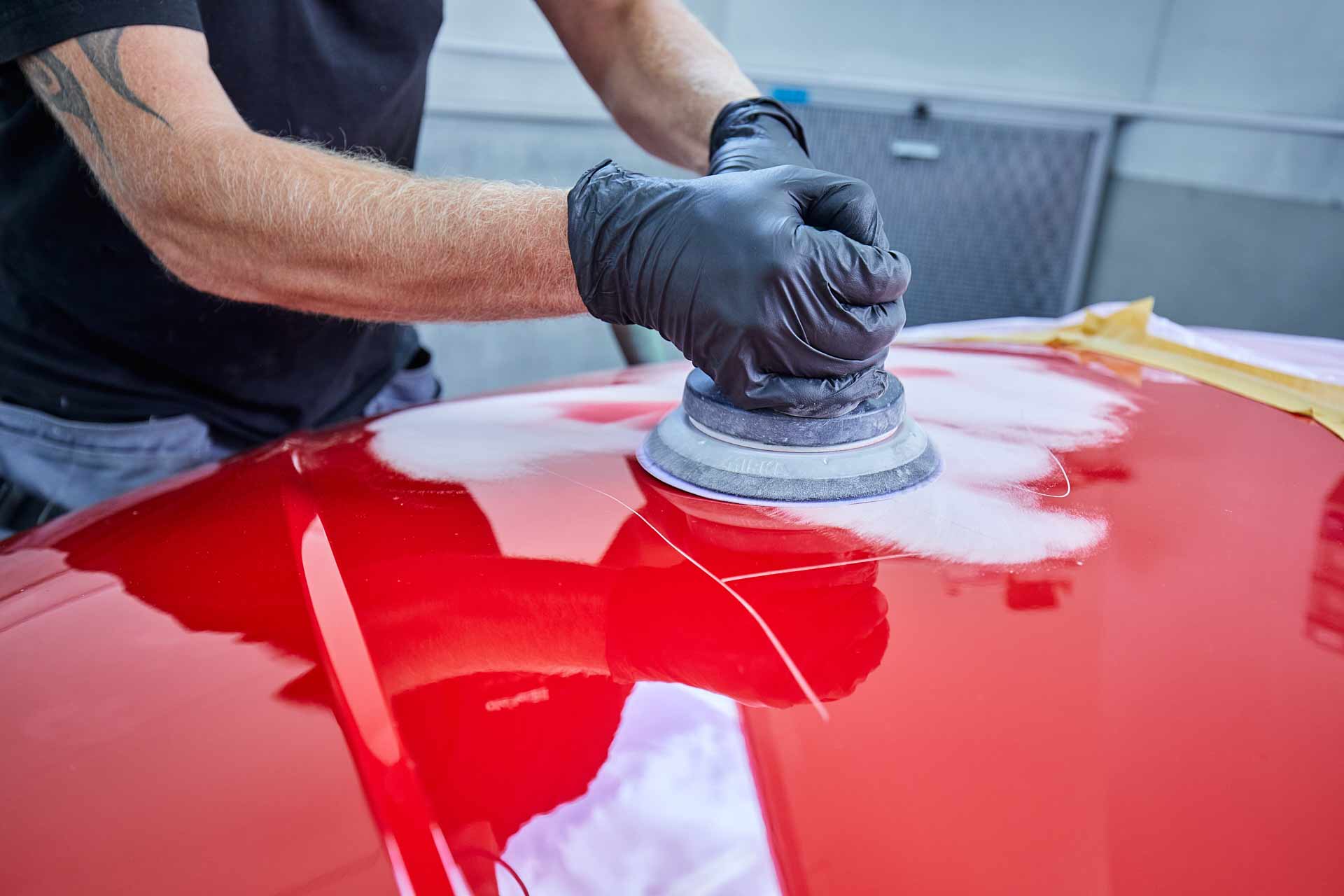 Medarbetare hos Olofsson Bil slipar lack på röd motorhuv inför lackreparation. Foto Martin Ekwall.